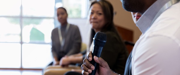 Panel discussion speaker holding microphone with panelists in background