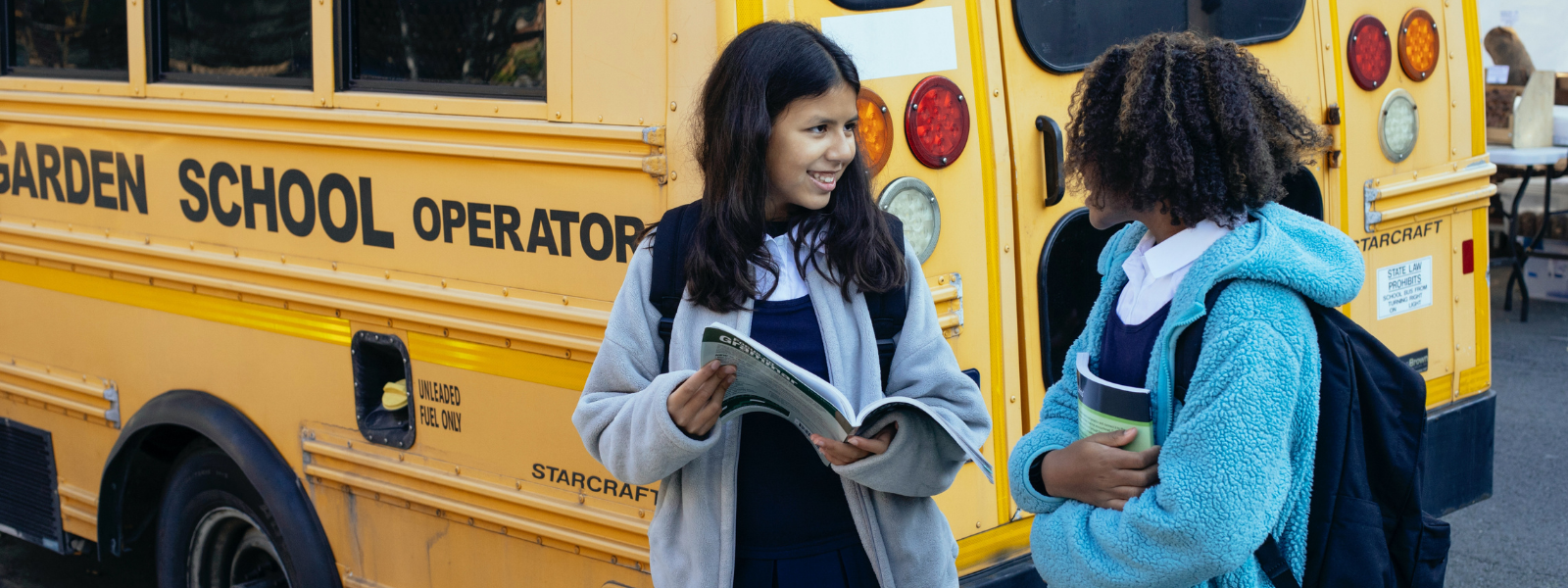 two girls with backpacks in front of a school bus