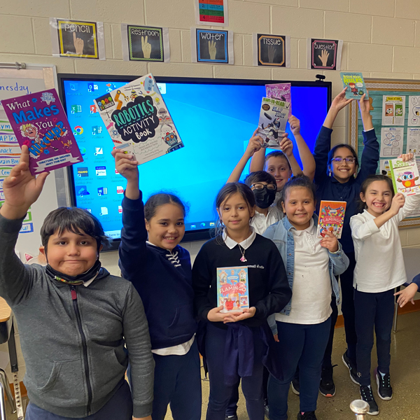 students in classroom holding up books