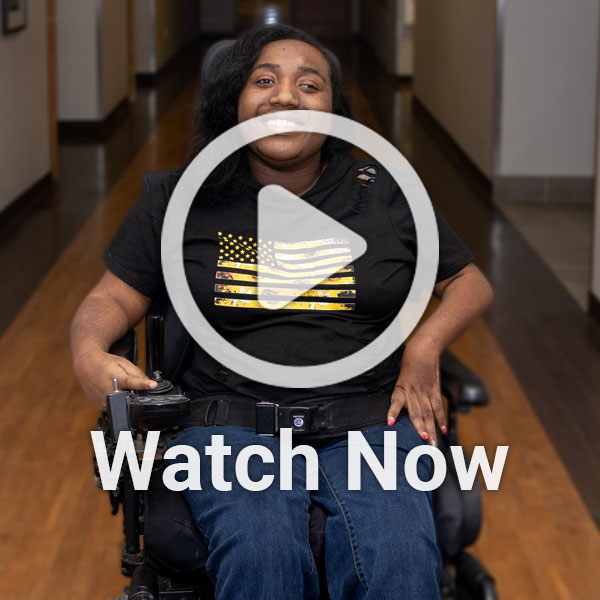 image of woman in wheelchair in hallway with a play overlay button